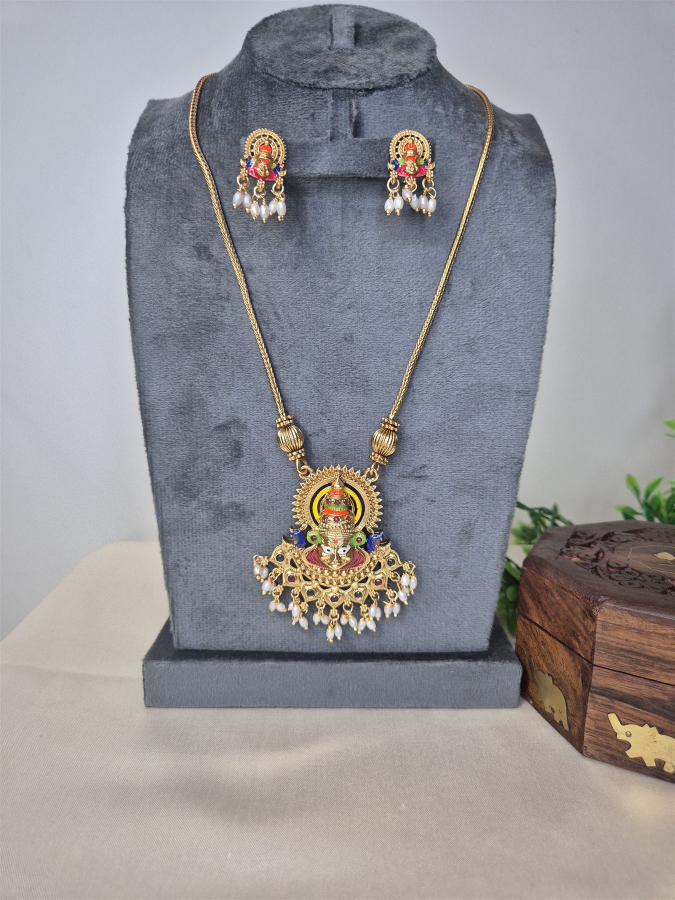 Temple-inspired pendant necklace and matching earrings displayed on a jewellery bust